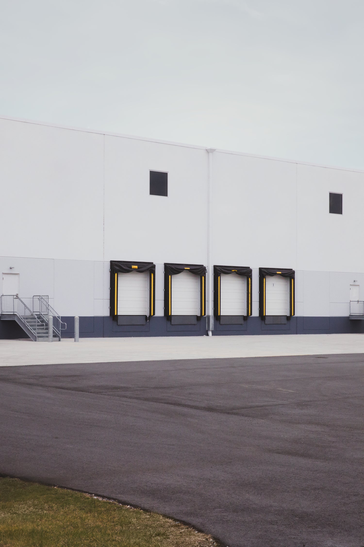A medium shot photo of the outside docking bay with 4 black and yellow trim doors of a white warehouse building. 